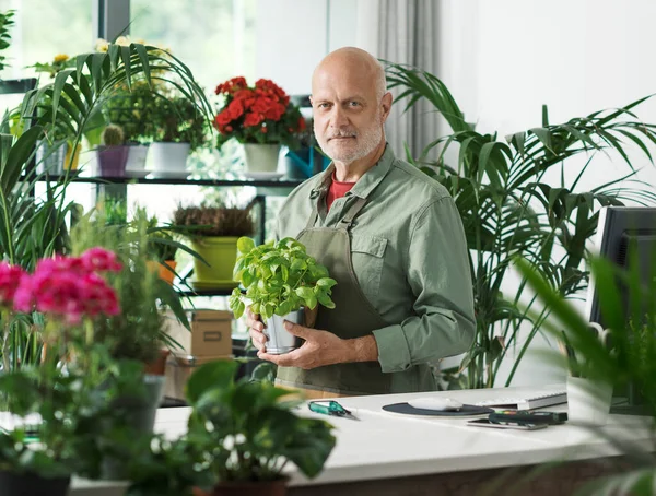 Professional florist and gardener posing in his plant shop, he is looking at camera, small business concept