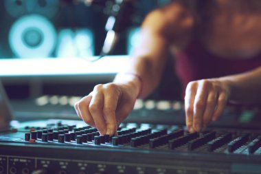 Genç müzisyen ses mikserini kayıt stüdyosuna kuruyor, eller yukarı.