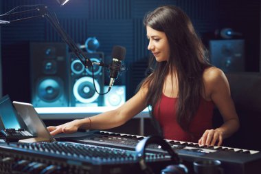 Kayıt stüdyosunda çalışan genç bir kadın dokunmatik ekran tableti kullanıyor ve şarkılar kaydediyor.