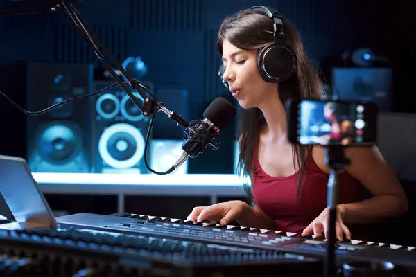 Young artist recording a song in the studio and shooting a video with her smartphone
