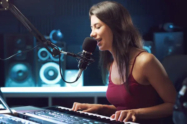 Young female artist singing and playing the keyboard in the recording studio, creativity and entertainment concept