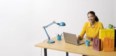 Masasında oturup bilgisayarında online alışveriş yapan genç bir kadın kredi kartıyla ödeme yapıyor.