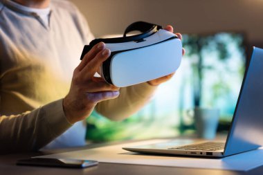 Evdeki masada oturan bir adam VR kulaklık, sanal gerçeklik ve teknoloji konsepti taşıyor.
