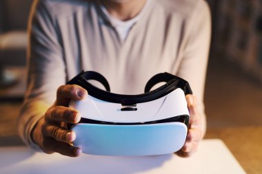 Masada oturan ve elinde sanal gerçeklik kulaklığı tutan bir adam.