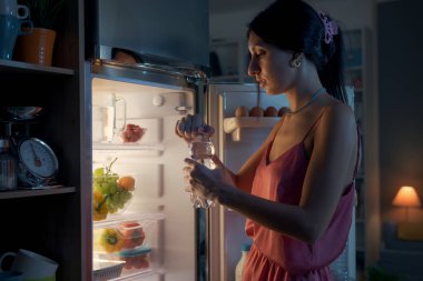 Susamış kadın geceleri buzdolabına bakıyor ve bir şişe su alıyor.