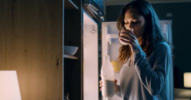 Susamış kadın buzdolabının önünde duruyor ve gecenin geç saatlerinde bir bardak süt içiyor.