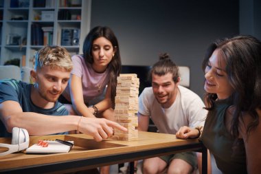 Bir grup genç birlikte evde vakit geçiriyorlar, Jenga oynuyorlar.