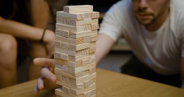 Arkadaşlar evde Jenga oynuyorlar, bir adam tahta bir blok tutuyor.