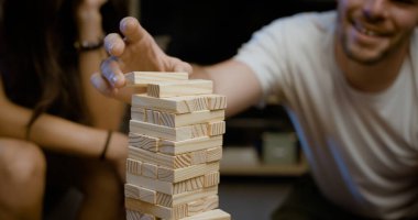 Arkadaşlar evde Jenga oynuyorlar, bir adam tahta bir blok tutuyor.