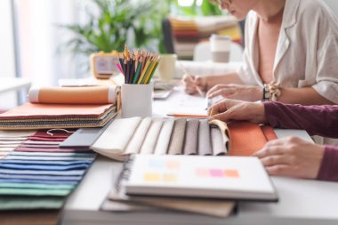 Profesyonel iç mimarlar ofislerindeki bir projede birlikte çalışıyorlar: kumaş örneklerini kontrol ediyorlar ve doğru renk paletini seçiyorlar, eller kapalı.