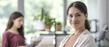 Ofisinde poz veren genç profesyonel tasarımcı gülümsüyor ve kameraya bakıyor.