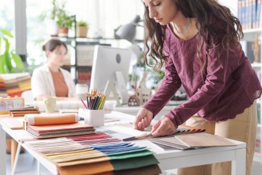 Ofiste çalışan profesyonel tasarımcı, yaratıcı projesi için kumaş örnekleri seçiyor.