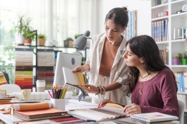 Genç iç mimarlar ofiste birlikte çalışıyorlar, kumaş örneklerini kontrol ediyorlar ve projeleri için mükemmel renk paletini seçiyorlar.