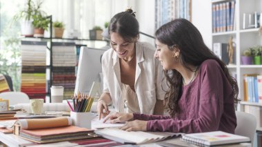 Ofisteki genç bayan iç mimar ve tasarımcılar bir proje üzerinde birlikte çalışıyorlar ve bir ev planını kontrol ediyorlar.