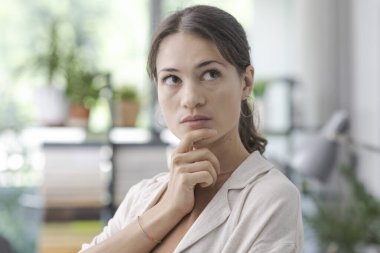 Kapalı alanda poz veren ve eli çenesinde düşünen genç bir kadın, karar ve fırsat kavramı.