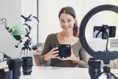 Sosyal medya için bir ürün değerlendirme videosu çeken genç içerik yaratıcısı, kameralar ve fotoğraf ekipmanları gösteriyor