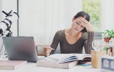 Genç öğrenci masada oturuyor ve kitap okuyor, yorgun ve bitkin.