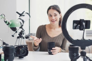 Sosyal medya için bir ürün değerlendirme videosu çeken genç içerik yaratıcısı, kameralar ve fotoğraf ekipmanları gösteriyor
