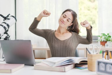 Evdeki masada oturup kollarını açarak mutlu bir öğrenci.