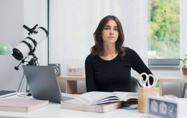 Kendine güvenen bir öğrenci evde masa başında oturmuş poz veriyor.