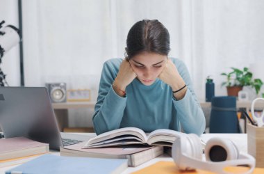 Akıllı kız evde masa başında oturuyor ve ders çalışıyor. Kitap okuyor, öğreniyor ve eğitim kavramını kavrıyor.