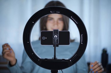 Genç yaratıcı kadın sosyal medyada takipçileri için canlı bir video yayınlıyor. Akıllı telefonunu ve halka lambasını kullanıyor.