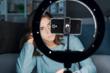 Evde sosyal medya için videolar yapan nüfuzlu bir kız akıllı telefon ve halka ışığı kullanıyor.