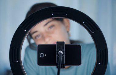 Genç yaratıcı kadın sosyal medyada takipçileri için canlı bir video yayınlıyor. Akıllı telefonunu ve halka lambasını kullanıyor.