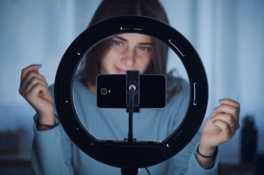 Genç yaratıcı kadın sosyal medyada takipçileri için canlı bir video yayınlıyor. Akıllı telefonunu ve halka lambasını kullanıyor.