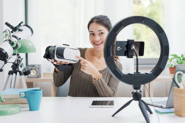 Создатель контента снимает видео дома для социальных сетей с помощью смартфона, она держит VR гарнитуру