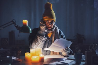 Kadın kendini üşümüş hissediyor ve doğal gaz ve elektrik tasarrufu için mum kullanıyor. Elektrik faturalarını kontrol ediyor ve tedarikçiyi arıyor.