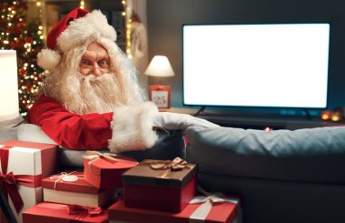 Noel Baba evde televizyon izliyor ve kameraya gülümsüyor. Kopya alanı olan boş bir televizyon ekranı.