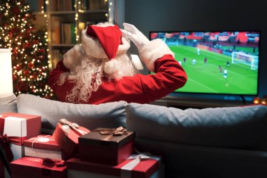 Neşeli Noel Baba evde kanepede dinleniyor ve televizyonda futbol seyrediyor, takımı kaybediyor.