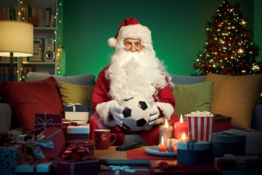 Mutlu Noel Baba evde dinleniyor ve Noel 'de futbol maçını seyrediyor, elinde bir futbol topu tutuyor.