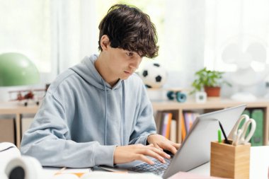 Akademik öğrenci evinde oturuyor ve bilgisayarını, teknolojisini ve online öğrenim konseptini kullanarak internete bağlanıyor.