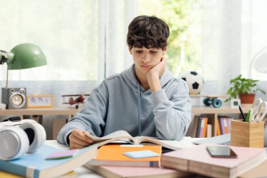 Zeki üniversite öğrencisi evde masa başında oturuyor ve kitap okuyor, o ev ödevi yapıyor.