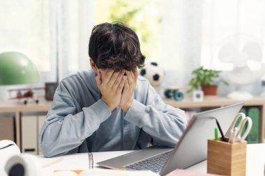 Yorgun, stresli bir öğrenci masasında oturuyor ve kafası ellerde dinleniyor, ergenlik sorunları kavramı.