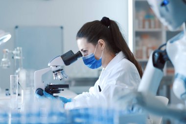 Laboratuvarda çalışan bilim adamı ve yapay zeka robotu: kadın mikroskop altındaki örneklere bakıyor ve robot ona yardım ediyor.