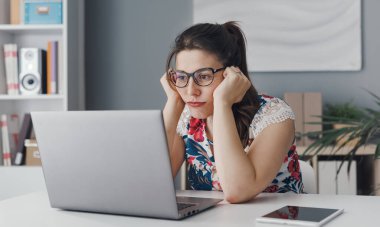 Sıkıcı üzgün kadın masasında oturup dizüstü bilgisayarına bakıyor.