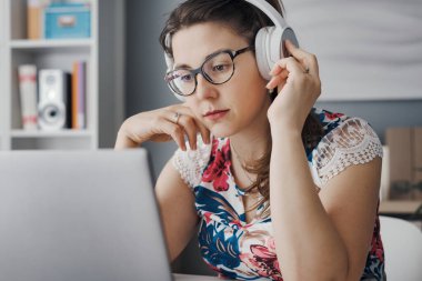 Kulaklık takan ve bilgisayarında video izleyen genç bir kadın.