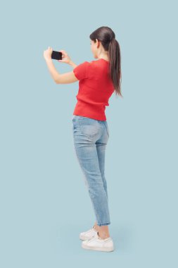 Akıllı telefon kullanan ve fotoğraf çeken genç bir kadın, arka plan, tam boy