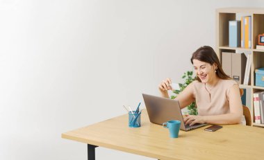 Masasında oturmuş dizüstü bilgisayarında komik videolar izleyen neşeli bir kadın gülümsüyor ve gülüyor.