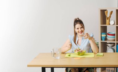 Sağlıklı bir salata ve bir bardak su içen mutlu kadın kameraya gülümsüyor.