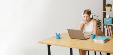 Masada oturan ve internetten video izleyen genç bir kadın, kulaklık takıyor ve bilgisayar ekranına bakıyor.