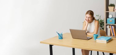 Genç gülümseyen kadın masada oturuyor ve internetten bilgisayarına bağlanıyor. İnternetten videolar izliyor.