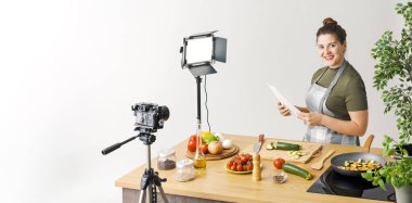 Gülümseyen profesyonel youtuber yemek videosu çekiyor, elinde bir çarşaf tutuyor ve gülümsüyor.