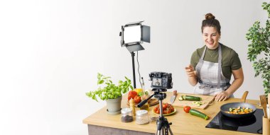 Gülümseyen profesyonel youtuber yemek pişirme videosu çekiyor, kameraya konuşuyor.
