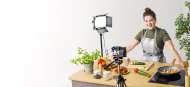 Gülümseyen profesyonel youtuber yemek videosu çekiyor, kameranın önünde sebze kesiyor.