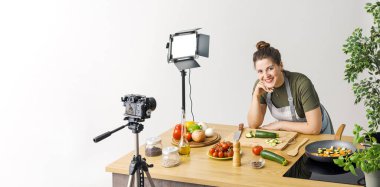 Gülümseyen profesyonel youtuber yemek videosu çekiyor, kameranın önünde sebze kesiyor.