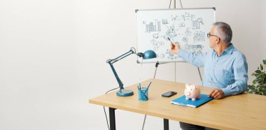 Ofiste bir sunum yapan profesyonel mali danışman ve işadamı, beyaz tahtaya işaret ediyor.